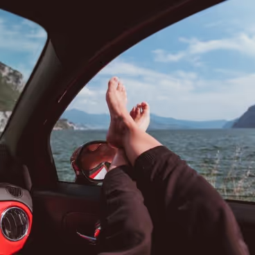 Persona con los pies descalzos encima de la ventanilla del coche