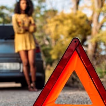Chica con coche averiado con el triángulo de emergencia