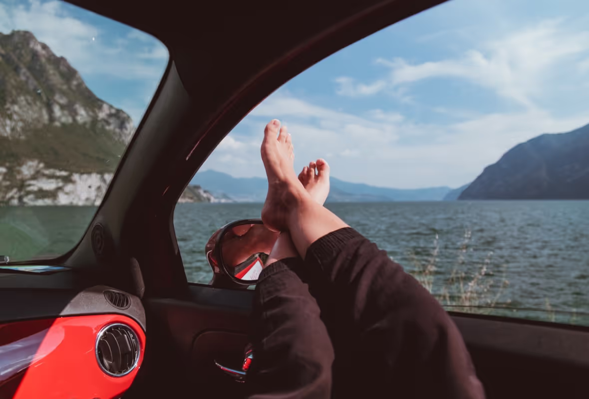 Persona con los pies descalzos encima de la ventanilla del coche